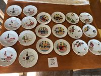 A wide shot of the 20 plates displayed on a wooden table showing varied designs of food, wine, storefronts and fruits.