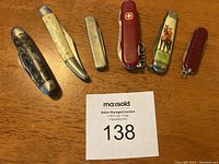 Top down view of all six pocketknives on wooden surface, showing diversity in size, color and design.