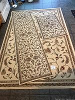 Photo showing all three rugs laid out on a tile floor: a large rug, a runner, and a smaller mat, all matching with ageless classic floral designs on a beige background.