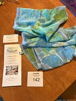 Silk scarf laid on wooden surface with artist and product information cards.