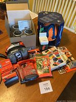 Overview photo showing all items in their packaging including monocle, hammock, socks, football, bivvy bags, safety vest, survival kits, mason jars and lights.