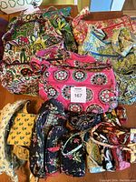 Top view of multiple Vera Bradley bags in various floral and colorful patterns, showing assortment of bags and pouches