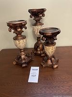 Photo of three decorative candle sticks of varying heights with ceramic tile mosaic bases and bronze ornamental details.