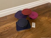 Five Pyrex glass storage dishes with assorted colored lids on wood floor