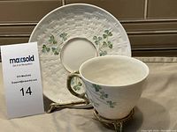 Tea cup and saucer displayed on a metal stand showing the shamrock motif and basket-weave detail on saucer.