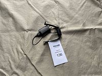 Black Fitbit charger cable on beige fabric background with MaxSold auction tag