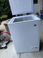 Close-up side view of the chest freezer with the lid open showing interior storage compartment and wire basket.