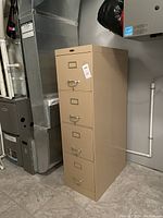 Full view of beige metal filing cabinet with 4 drawers shown next to HVAC system in a room.