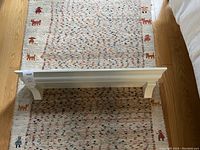 White wooden shelf with attached hanging brackets placed on colorful woven rug on hardwood floor