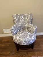 Front three-quarter view of swivel cushioned chair showing patterned upholstery, curved back, armrests, round seat and wood base.