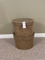 Two oval wicker baskets stacked one on top of the other with lids, showing woven texture and natural color.