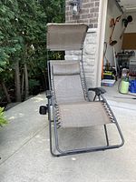 Zero gravity outdoor lounge chair with metal frame, mesh fabric seating, attached shading canopy overhead, and removable headrest pillow.
