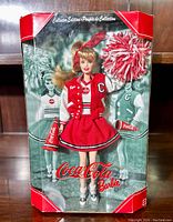 Front view of Barbie doll in original box showing doll in cheerleading outfit with pom pom and megaphone with Coca-Cola branding.