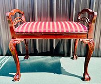 Front view of carved wooden bench with red striped upholstery, showing detailed claw feet and arms.