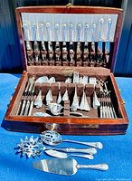 Wooden chest open showing full flatware collection with knives in lid and forks, spoons, servers in base