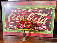 Photo of stained glass Coca-Cola lamp in front of vintage Coca-Cola advertising sign showing overall lot contents.