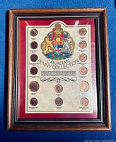 Framed display showing the obverse and reverse sides of several Canadian pennies arranged around the Canadian coat of arms on a red background.