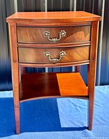 Front view showing wood grain, two drawers with ornate brass handles, and lower shelf.