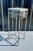Full side view showing squared granite-top and ornate metal frame with scroll and floral designs.