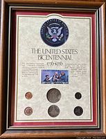 Full frontal view of the framed collection showing the coins and stamps arranged on a printed background with United States seal and text.