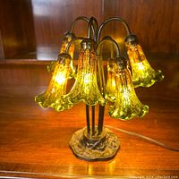 Full view of the lamp powered on, showing six yellow-green tulip-shaped art glass shades glowing warmly with crackled texture glass and bronze-tone metal stems.