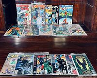 Photo shows a variety of Batman and Robin comics displayed on a wooden surface. Comics include several sealed in protective bags and holo cards.