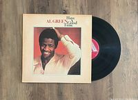 The vinyl LP record partially out of its album cover, showing the record's black surface and red label. The album cover features a photo of Al Green smiling, wearing a white shirt, with the album title on the front.