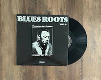 Black vinyl LP record 'Blues Roots Vol. 6' by Champion Jack Dupree with album sleeve showing black and white portrait on wooden surface.