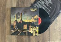 Photo of Pink Floyd Animals vinyl record partially out of jacket, showing front cover with flying pig above industrial plant and red label on the vinyl disc.