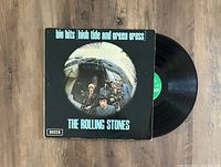 Photo of The Rolling Stones Big Hits (High Tide and Green Grass) LP vinyl record and album cover showing front artwork and vinyl record partially pulled out. The cover shows minor edge wear and the record label is green Decca.