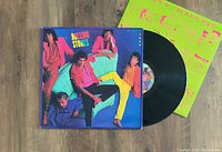 Photo of The Rolling Stones Dirty Work vinyl record partially pulled from its cover, displaying colorful cover art and the black vinyl disc alongside the neon green inner sleeve.