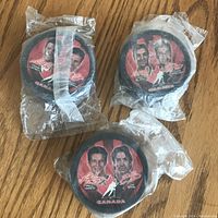 Three 2002 McDonald's Canada hockey pucks in sealed plastic packaging with player images and signatures visible on the puck tops.