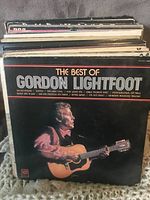 Photo of the front covers of a stack of vinyl LP records, highlighting 'The Best of Gordon Lightfoot' as the top album with other records behind it.