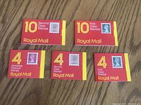 Top-down view showing all 5 unopened Royal Mail stamp booklets arranged on a wood surface.