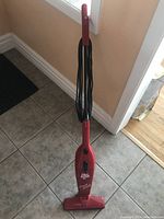 Full upright red Dirt Devil Swift Stick vacuum cleaner on tiled floor with power cord wrapped on holder.