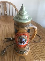 Front view of Holsten Brauerei beer stein with visible electric cord, showing detailed logo and metal lid