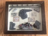 Full view of the shadow box showing all miniature biker items displayed against a white wood background inside a wooden frame.