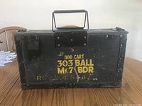 Front view showing stenciled yellow text '300 CART .303 BALL MK 7 BDR' on the rectangular black metal box with visible wear and riveted reinforcement.