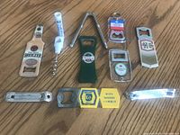 Assorted vintage bottle and can openers and a metal nutcracker arranged on a wooden surface showing various brands and styles of openers.