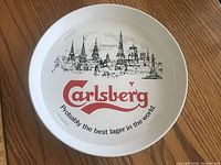 Front side of the round metal bar tray showing detailed sketch of Copenhagen skyline, Carlsberg logo, and tagline.