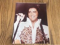 Front side of vintage 8x10 color photograph of Elvis Presley in costume on stage, holding microphone and guitar, smiling.