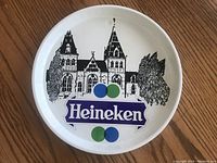 Front view of round metal tray featuring Heineken logo and building illustration on white background