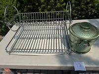 Photo of the aluminum dish drying rack and covered green metal ice bucket on a white surface outdoors.