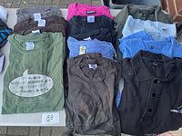 Top view of assorted folded men's shirts showing a mix of collared button-up shirts and printed T-shirts in various colors including black, blue, brown, green, and grey.