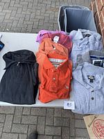 Lot of six men's fleece and knit tops including different colors and brands presented folded on a table outdoors