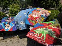 Four children's sleeping bags displayed outdoors with various cartoon character and dinosaur designs