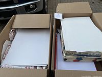 Two cardboard boxes filled with white blank paper sheets, some stacks are not opened.