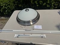 Round ceiling light fixture with frosted glass dome and metal trim, shown on a table outdoors