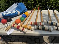 Full croquet set arranged on table outdoors showing mallets, balls, wickets, stakes, and carrying bag