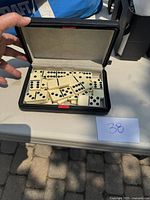 Opened black carrying case showing white domino pieces with black dots inside, lining visible